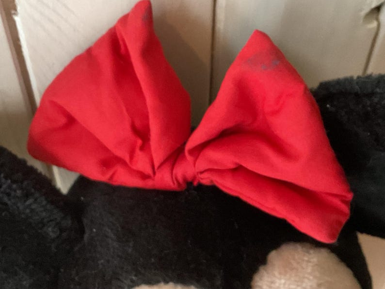 May include: A vivid red bow, possibly made of fabric, is the central element, set against a black and white background. The bow's bright colour provides a contrast to the darker tones, creating a visually striking image. The bow's shape suggests it could be part of a larger item.