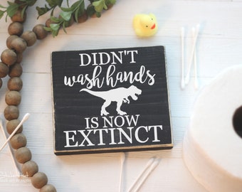 Könnte beinhalten: Schwarzes Holzschild mit weißem Text, der "Didn't wash hands is now extinct" lautet. Über dem Text befindet sich eine weiße Silhouette eines Tyrannosaurus Rex.