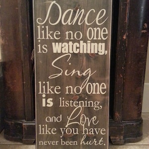 May include: A wooden sign with a white painted message that reads "Dance like no one is watching, Sing like no one is listening, and Love like you have never been hurt."