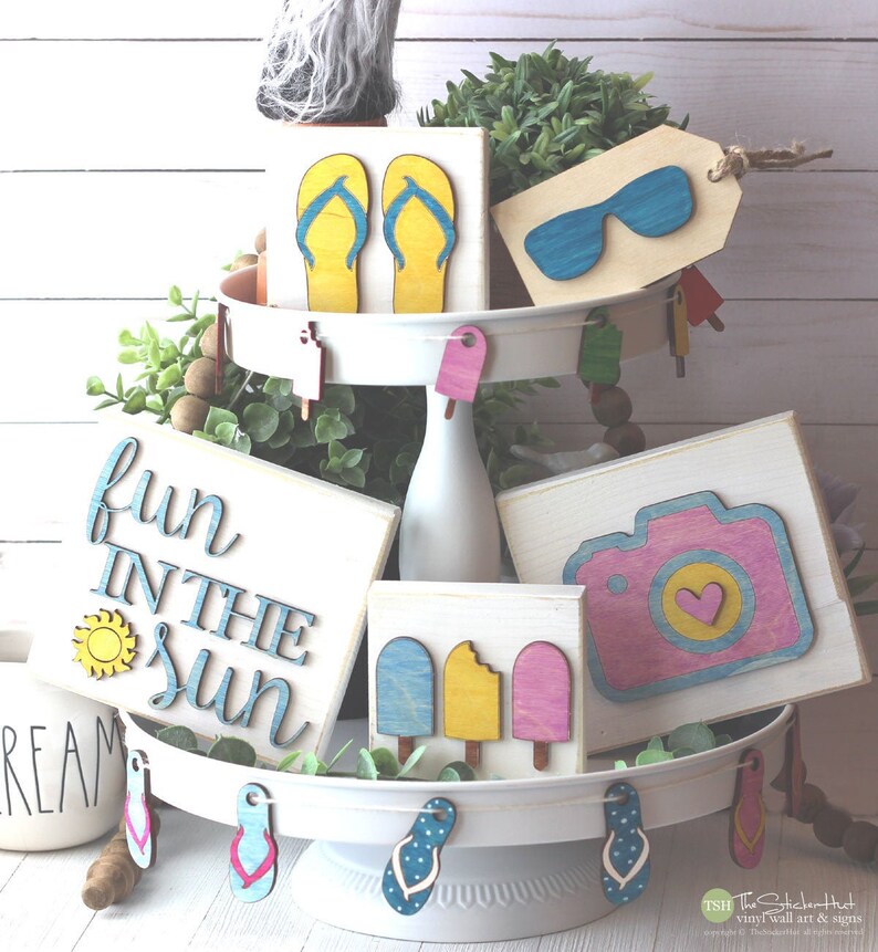 May include: A tiered tray decorated with summer-themed wooden signs. The signs feature flip flops, sunglasses, ice cream, a camera, and the text "Fun in the Sun".
