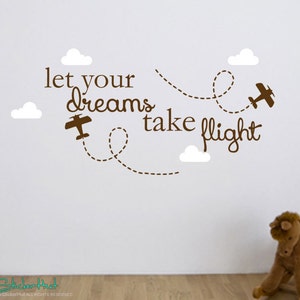 May include: Brown wall decal with the text "let your dreams take flight" and two airplanes with dotted lines representing flight paths. There are white clouds around the text and airplanes.