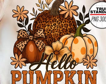 Könnte beinhalten: Cremefarbenes T-Shirt mit einem herbstlichen Motiv. Das Design zeigt Kürbisse, Blumen und den Text "Hello Pumpkin" in Braun. Das Design umfasst einen Kürbis mit Leopardenmuster und eine Jack-o'-Lantern-Tasse.