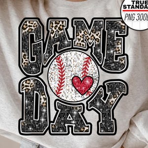 May include: A light gray sweatshirt with the words "GAME DAY" in a black, leopard print, and glitter design. A baseball with red stitching and a red heart is in the center of the design. A white circle with text is in the upper right corner.