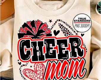 Puede incluir: Una sudadera blanca con un diseño rojo, negro y blanco que dice "Cheer Mom". El diseño incluye un pompón, un corazón y un estampado de leopardo.