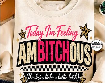 Może przedstawiać: Kremowa bluza z napisem "Today I'm Feeling AMBITCHOUS" w kolorze różowym i czarnym, z akcentami w postaci gwiazd w panterkę. Pod głównym tekstem znajduje się fraza "(the desire to be a better b*tch)".