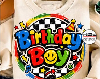 Puede incluir: Sudadera color crema con un gráfico colorido de "Birthday Boy". El diseño incluye una carita sonriente, estrellas, rayos y un fondo a cuadros. El texto está en letras en negrita y multicolores.