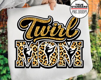 Puede incluir: Sudadera blanca con la frase "Twirl Mom". La palabra "Twirl" es de purpurina dorada con contorno negro. "MOM" tiene un estampado de leopardo con siluetas de bastoneras.