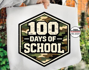 Puede incluir: Camiseta blanca con un diseño hexagonal grande con el texto "100 DAYS OF SCHOOL". El diseño incorpora un patrón de camuflaje en tonos verdes, marrones y beige, con bordes negros y letras blancas. Se ve un pequeño logotipo circular.
