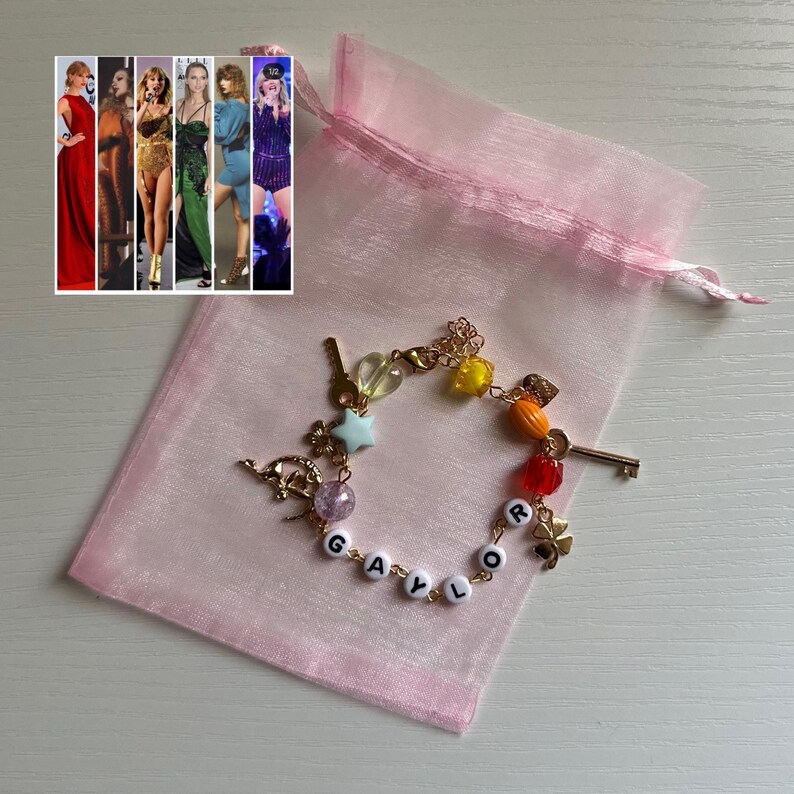 May include: A gold-colored charm bracelet with colorful beads and charms, including a key, stars, and a four-leaf clover. The bracelet spells out "GAYLOR" with white letter beads. A pink organza bag and a collage of images are in the background.