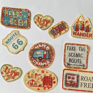 May include: A set of ten colourful fabric patches with various designs and text, including "Beep Beep", "I Love Travel", "Route 66", "Road Trip", "Wander", "Happy Camper", "Let's Go", "Take the Scenic Route", "Roam Free".