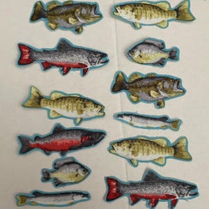 May include: A collection of fabric fish patches in various shapes and sizes. The patches feature detailed designs with shades of brown, gray, red, and yellow, outlined in light blue. These patches are ideal for crafting and adding a unique touch to clothing or accessories.