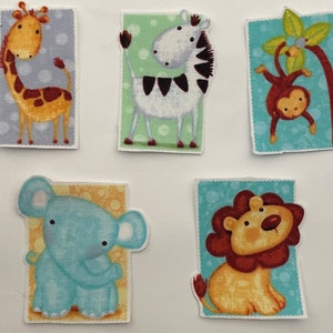 Peut inclure: Cinq écussons en tissu avec des animaux de dessins animés : une girafe, un zèbre, un singe, un éléphant et un lion. Chaque animal est placé sur un fond rectangulaire avec un motif. La girafe et le zèbre sont debout, le singe est suspendu à un arbre.