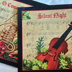 May include: Two Christmas-themed cards with musical instrument illustrations. One features a French horn with a red bow and the words "O Come". The other card displays a violin and the words "Silent Night" with musical notes and holly.