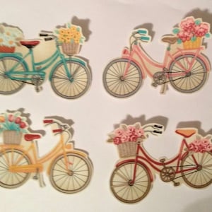 May include: Four decorative bicycle cutouts, each with a basket of flowers. The bicycles are in various colors: teal, pink, yellow, and red. The wheels and frames are detailed, and the baskets are filled with different flower arrangements.