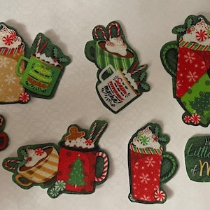May include: Nine festive Christmas-themed fabric patches featuring mugs of hot chocolate with whipped cream and candy cane stirrers. The patches are decorated with snowflakes, holly, and the phrase "Have a Little Cup of Merry".