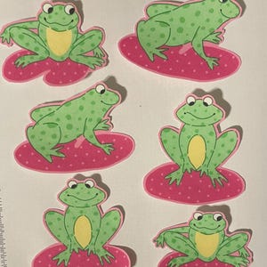 May include: Five green frog stickers with yellow bellies on pink lily pads with white polka dots. The frogs have green spots and are in various poses.