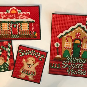 以下が含まれることがあります： ジンジャーブレッドハウスのデザインが施された、クリスマスをテーマにした、お祝いのファブリック正方形が4つあります。1つの正方形には、ドアの上に「General Store」という文字が書かれたジンジャーブレッドハウスがあります。もう1つの正方形には、「Welcome Sweet Home」という文字が書かれたジンジャーブレッドハウスがあります。他の2つの正方形には、キャンディーケーンを持ったジンジャーブレッドマンが描かれています。