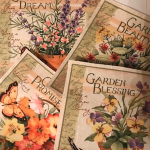 May include: Four square fabric coasters with floral designs and text. The coasters feature different floral arrangements, including lavender, yellow flowers, and red flowers. The text on the coasters includes "Garden Dream", "Garden Beauty", "Garden Blessing", and "Garden Promise".