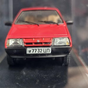 Puede incluir: Un coche rojo en miniatura con parachoques delantero y faros negros. El coche tiene una matrícula con el texto "И 7732 ЦП". El coche es un modelo de un vehículo clásico.