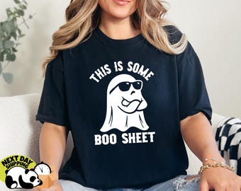 May include: Black t-shirt with a white graphic of a ghost wearing sunglasses and the text "THIS IS SOME BOO SHEET". The shirt is a Halloween-themed design.