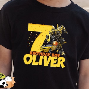 May include: Black t-shirt with a yellow number 7, a yellow car, a yellow robot, and the text "Birthday Boy Oliver".