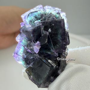 Könnte beinhalten: Nahaufnahme eines Fluorit-Kristallclusters. Der Kristall weist einen tiefvioletten Farbton mit schillernden blauen und grünen Reflexen auf. Die geometrische Struktur des Kristalls ist deutlich sichtbar und zeigt seine natürliche Entstehung.