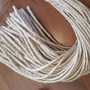 Może przedstawiać: Paczka jasnoblond syntetycznych dredów. Dredy są wykonane z włosów kanekalonowych i mają około 50 cm długości.