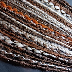 May include: A collection of brown, white and orange synthetic dreadlocks. The dreadlocks are braided together and have a white string woven through them.