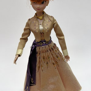 May include: A doll with red hair wearing a gold and brown dress with purple accents. The dress has a gold belt and intricate details.