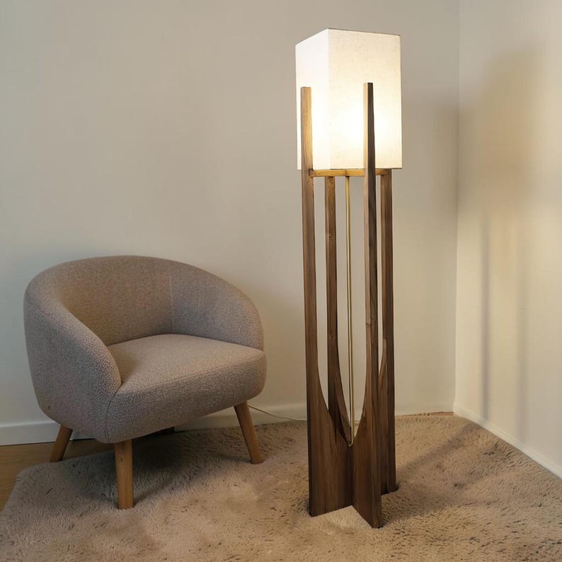 Puede incluir: Una l&aacute;mpara de pie moderna con una pantalla rectangular blanca y una estructura de madera oscura. La l&aacute;mpara tiene un dise&ntilde;o &uacute;nico con soportes verticales de madera y un acento de lat&oacute;n. Un sill&oacute;n beige est&aacute; cerca.