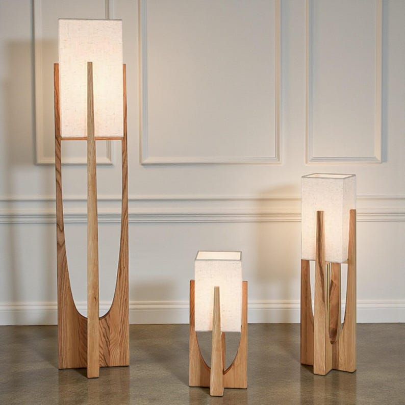 Puede incluir: Tres l&aacute;mparas de madera con pantallas rectangulares de color blanco roto. Las l&aacute;mparas tienen un acabado de madera natural y un dise&ntilde;o &uacute;nico de marco abierto. Las l&aacute;mparas var&iacute;an en altura, destacando la m&aacute;s alta. Las pantallas emiten un brillo suave y c&aacute;lido.