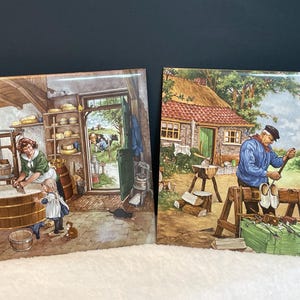 May include: Two ceramic tiles with Dutch village scenes. One depicts a woman and child in a cheese-making room, the other shows a man crafting wooden shoes. The tiles feature detailed illustrations with vibrant colors.