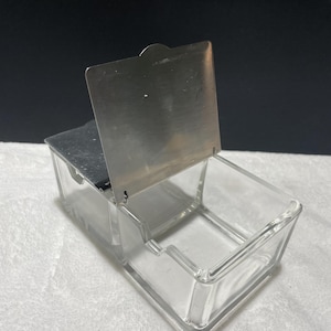 May include: A clear glass box with a hinged metal lid. The lid is open and the box is empty.