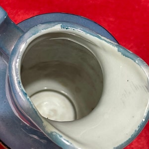 Op de afbeelding: Een blauwe en witte keramische kan met een zilveren rand. De kan heeft een brede opening en een handvat.