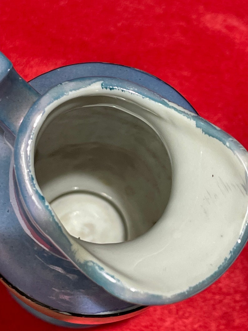 Op de afbeelding: Een blauwe en witte keramische kan met een zilveren rand. De kan heeft een brede opening en een handvat.