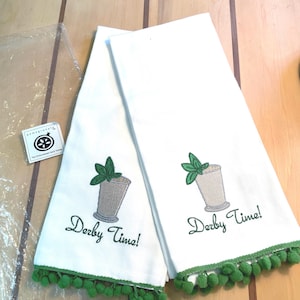 May include: Two white kitchen towels with green pom-pom trim. Each towel features an embroidered mint julep glass with a sprig of mint and the text "Derby Time!"