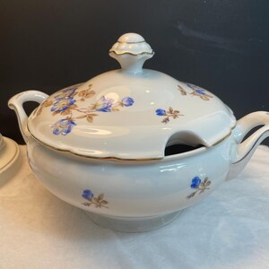 May include: White porcelain soup tureen with a lid, decorated with blue and brown floral patterns and gold trim. The tureen has two handles and a ladle opening. A classic piece for serving soup.
