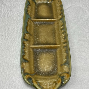 May include: A ceramic serving dish with three divided sections. The dish is glazed in a light brown color with a green glaze around the edges.