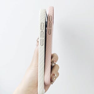 May include: Two rectangular smartphone cases held together, one in a textured off-white finish and the other in a textured light pink finish. Both cases feature precise cutouts for side buttons and a slim, protective profile for mobile devices.