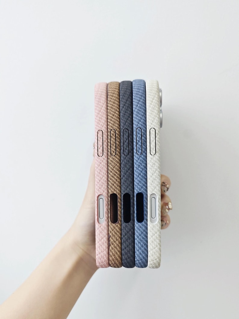 May include: A stack of five smartphone cases featuring a textured, woven fabric-like finish in shades of light pink, tan, dark gray, blue, and off-white. Each case has precise cutouts for side buttons and ports along the vertical edge.