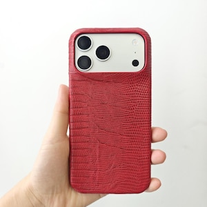 May include: A smartphone case with a textured red finish resembling lizard skin. The case features a rectangular cutout at the top to accommodate the three camera lenses and the flash module of the device, which has a white back panel.