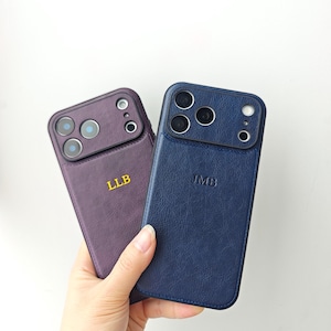 Puede incluir: Dos fundas para teléfono con textura de cuero, una en color morado oscuro con las iniciales LLB en amarillo y otra en azul marino con las iniciales JMB en relieve. Ambas fundas tienen un recorte rectangular para la cámara.