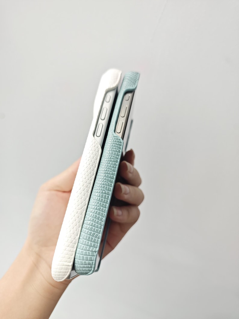 May include: Two smartphone cases with a textured, embossed pattern resembling reptile skin. One case is white and the other is a light blue-green colour. Both cases feature cutouts for side buttons and are shown from a side profile view.