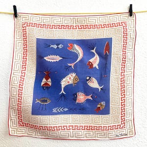 Könnte beinhalten: Quadratischer Stoff mit blauem Mittelteil und stilisierten Fischmotiven. Der Stoff hat einen roten Rand und ein sich wiederholendes geometrisches Muster. Die Fische in verschiedenen Farben und Mustern bilden ein lebendiges Textil.