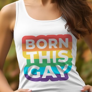May include: White tank top with the text "BORN THIS GAY" in rainbow colors. The text is stacked vertically, with each word in a different color of the rainbow. The tank top is a casual style.