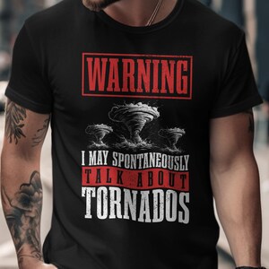 May include: Black t-shirt with a graphic design featuring three tornadoes and the text "WARNING I MAY SPONTANEOUSLY TALK ABOUT TORNADOS" in white and red. The shirt has a crew neck and short sleeves.