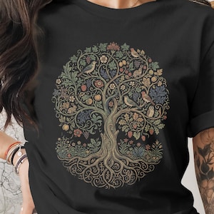 May include: Black t-shirt featuring a detailed, circular tree design. The tree has a complex root system, a brown trunk, and branches filled with leaves, flowers, and birds in shades of green, blue, and red. The design is centered on the shirt.