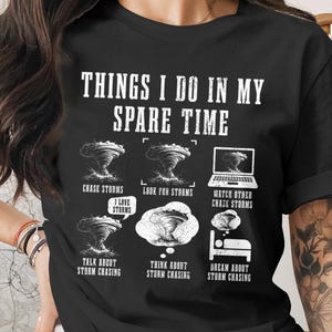 Puede incluir: Camiseta negra con el texto "THINGS I DO IN MY SPARE TIME" e ilustraciones de tornados, un portátil y una cama. La camiseta también incluye las frases "CHASE STORMS", "LOOK FOR STORMS", "WATCH OTHER CHASE STORMS", "TALK ABOUT STORM CHASING", "THINK ABOUT STORM CHASING" y "DREAM ABOUT STORM CHASING".