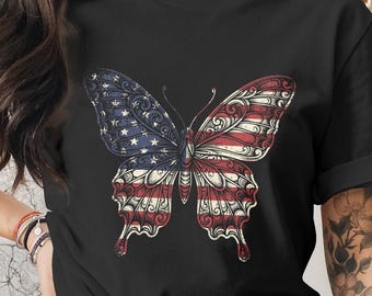 Peut inclure: T-shirt noir avec un motif de papillon détaillé. Les ailes du papillon sont divisées, un côté présentant les étoiles et les rayures du drapeau américain. L'autre aile reflète le motif. Le t-shirt a un col rond classique.