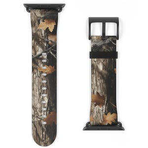 Könnte beinhalten: Ein Armband für eine Uhr mit Tarnmuster und einer schwarzen Schnalle und Anschlüssen. Das Armband zeigt ein braunes und beiges Baumrindenmuster mit verstreuten braunen Blättern und erzeugt eine natürliche Outdoor-Ästhetik. Das Armband ist für eine Smartwatch konzipiert.